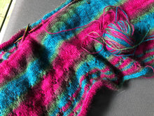 Load image into Gallery viewer, A piece of knitting on circular KnitPro knitting needles. 2ply hand-painted Merino/Possum/Silk yarn by Touch yarns in Macaw variant; tones of fuchsia pink, budgie green, teal green and deep purple. Cowl is knitted in the round with the yarn colours creating a large whirlpool of each colour around the cowl.
